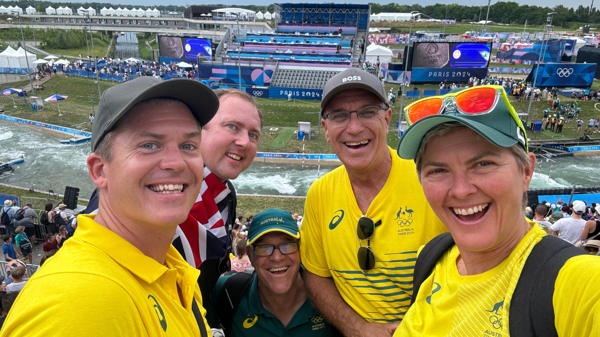 Nat Cook - Paris 2024 - in the stands watching Olympian Jess Fox in the canoe gold medal race. Nat is smiling and wearing green and gold for Australia.