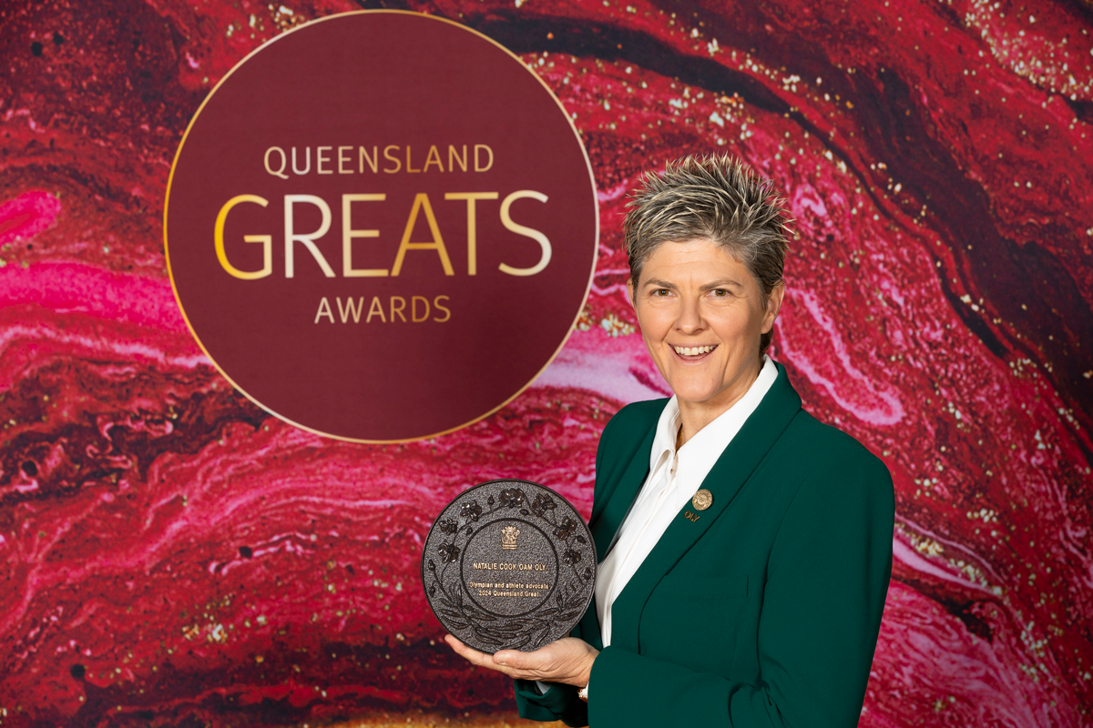 Natalie Cook OAM OLY smiling and holding her 2024 Queensland Greats Award plaque